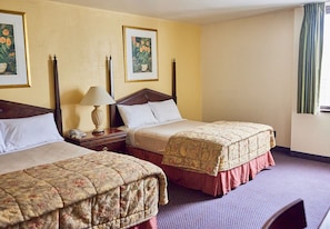 Habitación de hotel con dos camas individuales, una mesita de noche con lámpara y dos cuadros enmarcados con motivos florales en la pared.