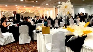 A banquet hall with round tables covered in white tablecloths, white chair covers, and a large white floral centerpiece. - The McLure Hotel and Conference Center (Wheeling)