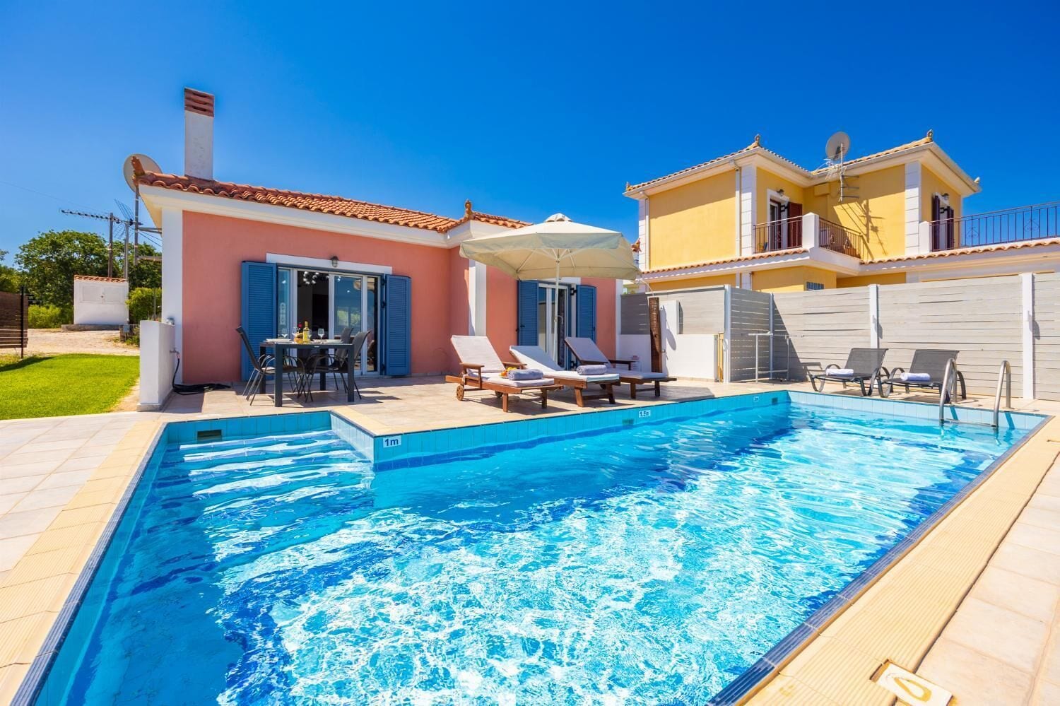 Ein Schwimmbad mit Liegestühlen und einem Tisch, umgeben von einem Haus mit einem Ziegeldach und einem Garten.