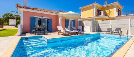 Ein Schwimmbad mit Liegestühlen und einem Tisch, umgeben von einem Haus mit einem Ziegeldach und einem Garten.