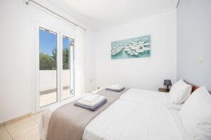 A hotel room with a bed, a painting, a nightstand, and a view through a sliding door.