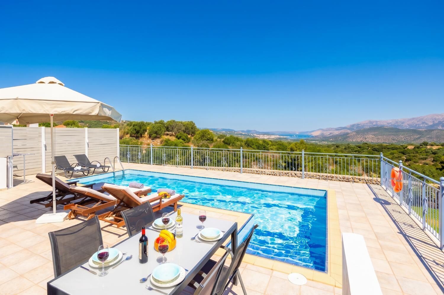 A poolside area with a table set for dining, lounge chairs, and a view of the landscape.