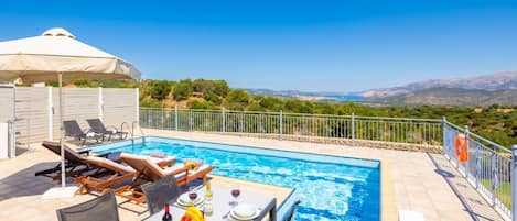 A poolside area with a table set for dining, lounge chairs, and a view of the landscape.