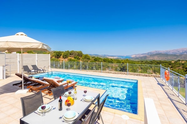 A poolside area with a table set for dining, lounge chairs, and a view of the landscape.
