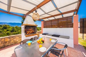 Un área de comedor al aire libre con una parrilla, mesa, sillas y vistas del paisaje.