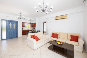 Una sala de estar con un juego de sofá, una mesa de centro con fruta y un comedor con una cocina al fondo.