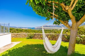Una hamaca colgada de un árbol en un jardín cuidado con un muro de piedra y una vista despejada de un paisaje montañoso.