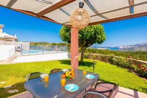 A table with a view of a swimming pool, a tree, and a landscape.