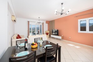 A dining area with a table set for four, a sofa, a TV, and a view of the outdoors. - Villa Europe Ena - Two Bedroom Villa, Sleeps 4 (Ionian Islands)
