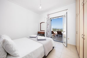 A bedroom with a bed, a nightstand, a dresser, and a balcony with a view. - Villa Europe Ena - Two Bedroom Villa, Sleeps 4 (Ionian Islands)