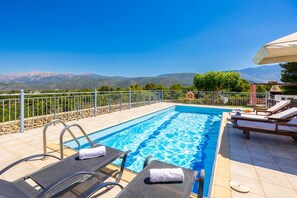 A swimming pool with a view of mountains, surrounded by a fence, and equipped with lounge chairs and a table.