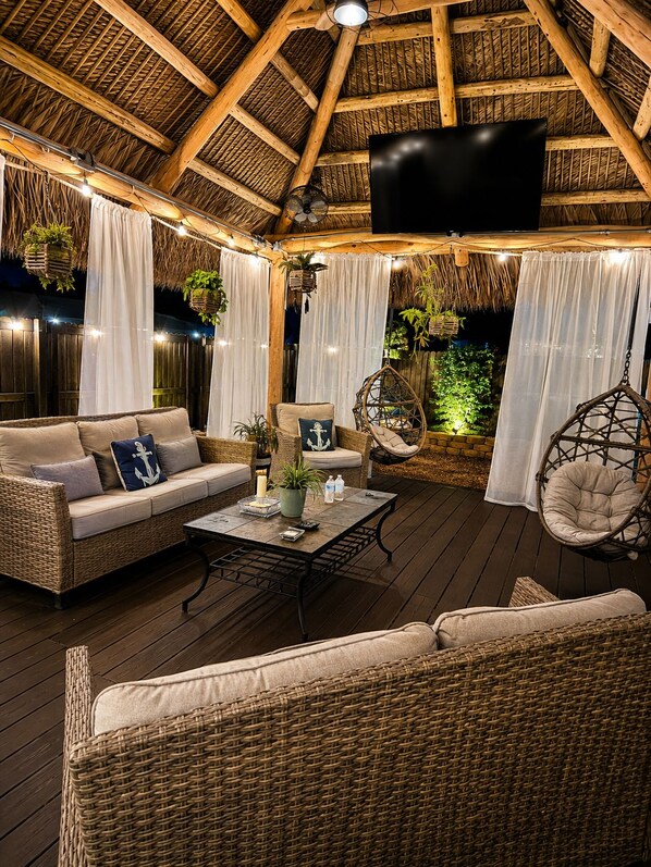 An outdoor seating area with wicker furniture, a hanging chair, and a ceiling fan.