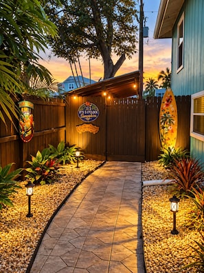 A wooden gate with a sign, a tiki bar sign, and a surfboard leaning against the fence.