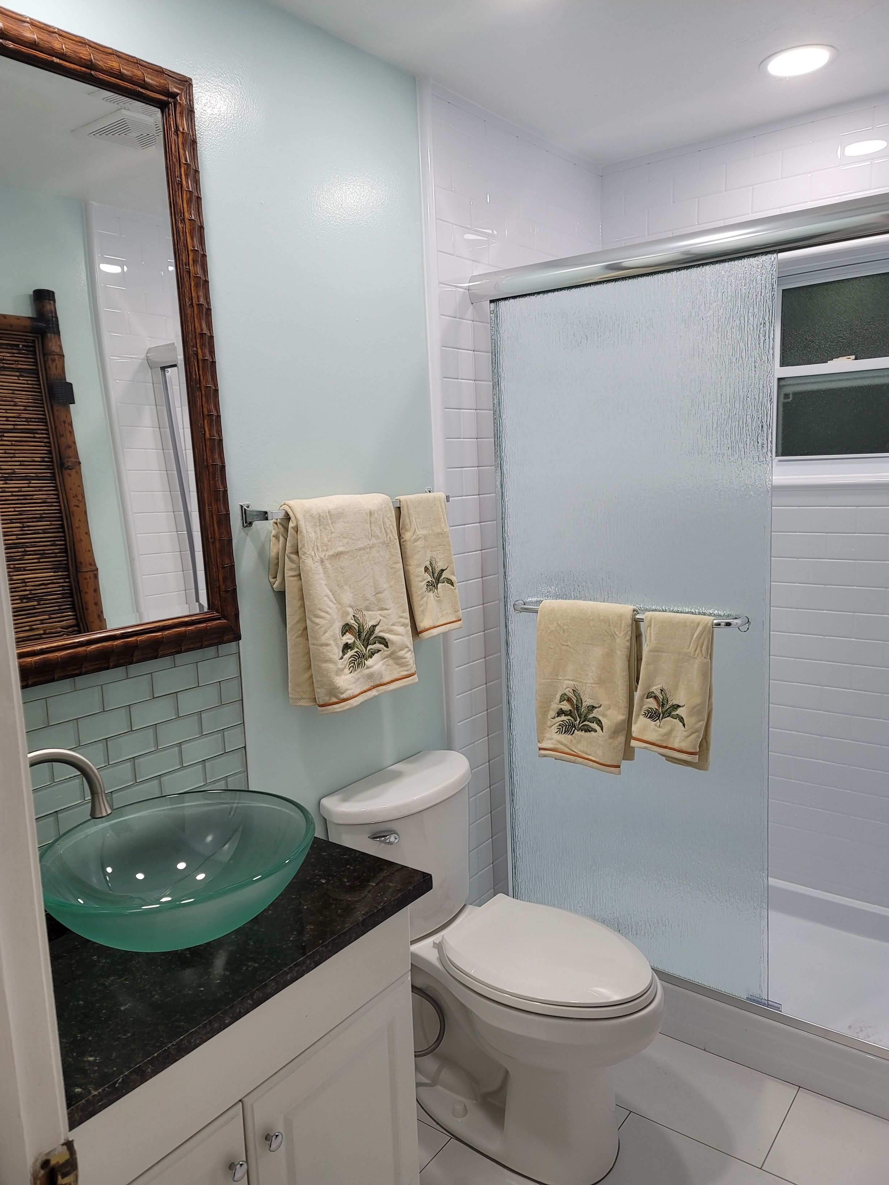 A bathroom with a glass sink, white toilet, and a shower with glass doors.