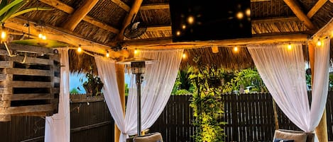 Een terras buiten met een houten plafond, rieten meubels en lichtjes.