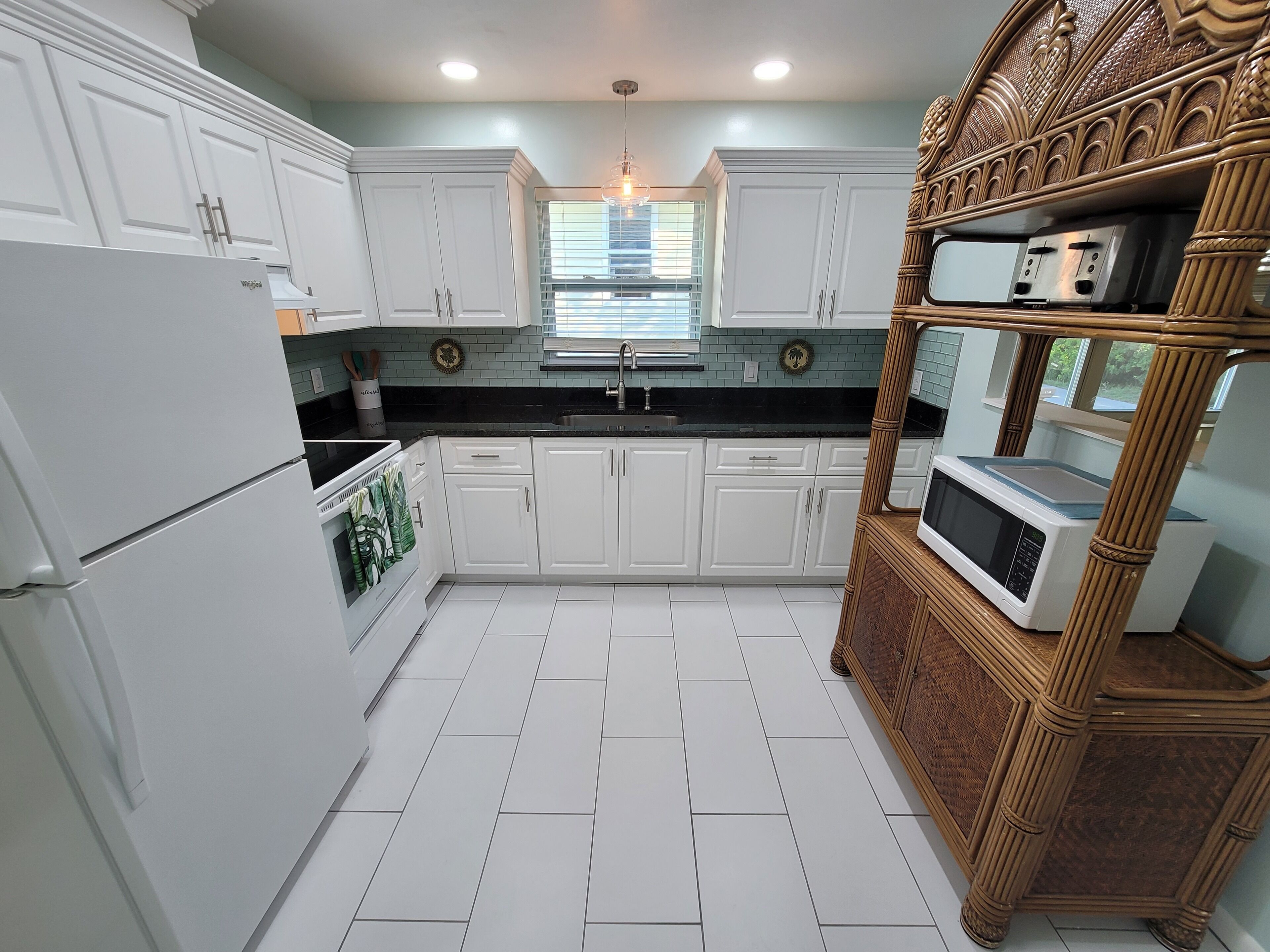 A kitchen with white cabinets, a black countertop, and a microwave on a wooden stand.