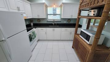 A kitchen with white cabinets, a black countertop, and a microwave on a wooden stand.