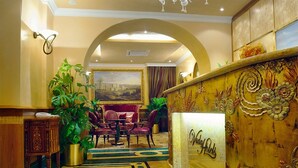 A hotel lobby with a chandelier, a reception desk, and a large painting on the wall. - Hotel Homs (Rome)
