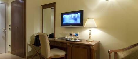 A hotel room with a wooden desk, a chair, a television, a lamp, and a mirror.