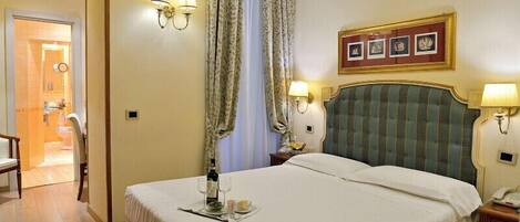 A hotel room with a large bed, two bedside lamps, a framed picture above the bed, and a small table with a bottle and glasses.