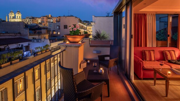 A balcony with wicker furniture, a red sofa, and a table with a glass of wine. - Hotel Homs (Rome)