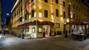 A hotel with a red awning, outdoor seating, and potted plants. - Hotel Homs (Rome)
