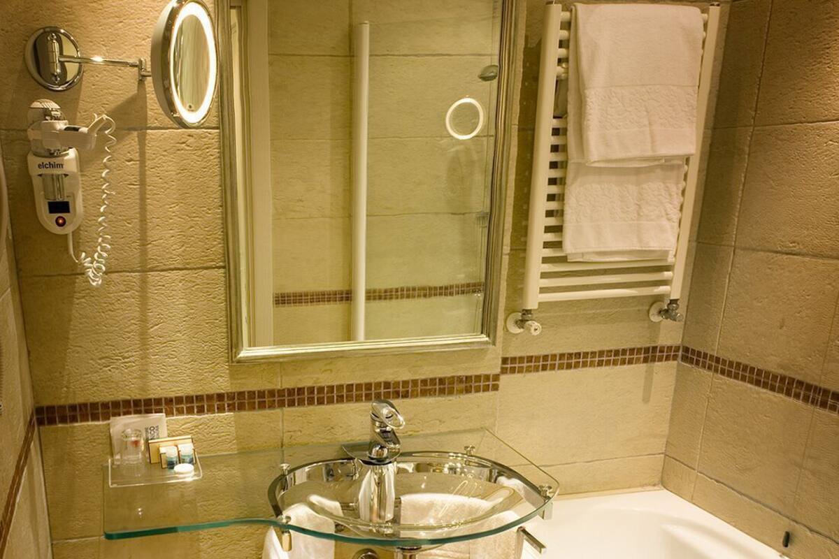 Un bagno con un water, un lavandino in vetro, una vasca e uno specchio.