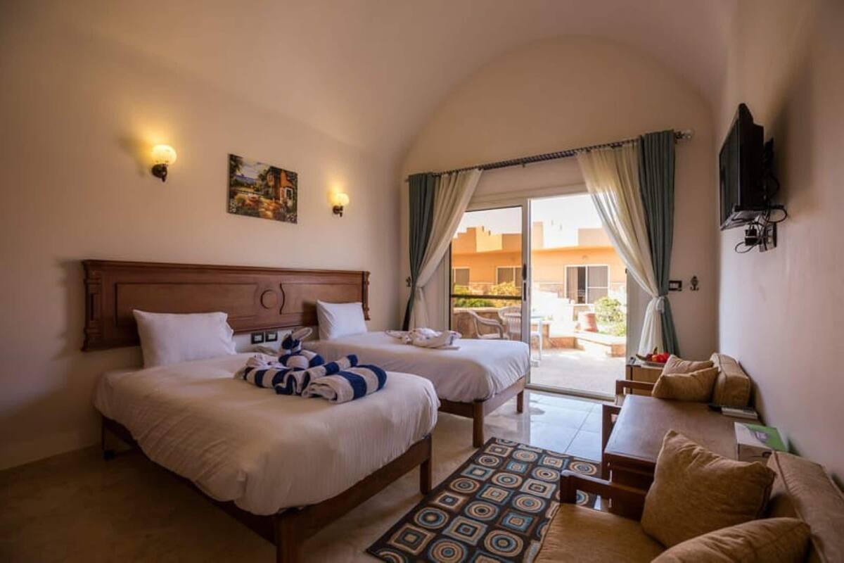A hotel room with two beds, a sofa, a TV, and a balcony with a view.