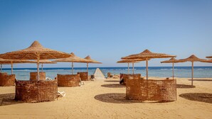 A beach with rows of wicker beach chairs and umbrellas, a clear sky, and the ocean in the background. - Silver Beach Boutique Hotel (El Quseir)