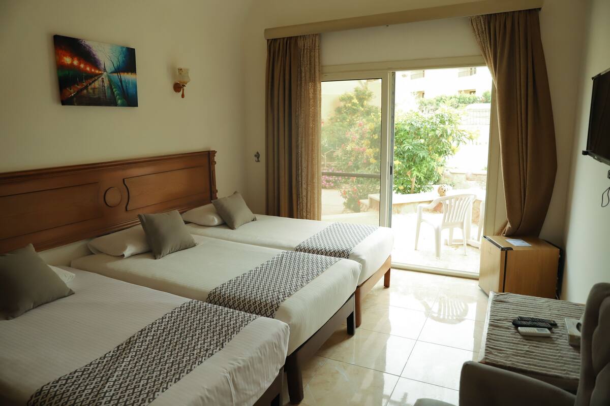 A hotel room with two beds, a desk, a chair, and a view of the outdoors.