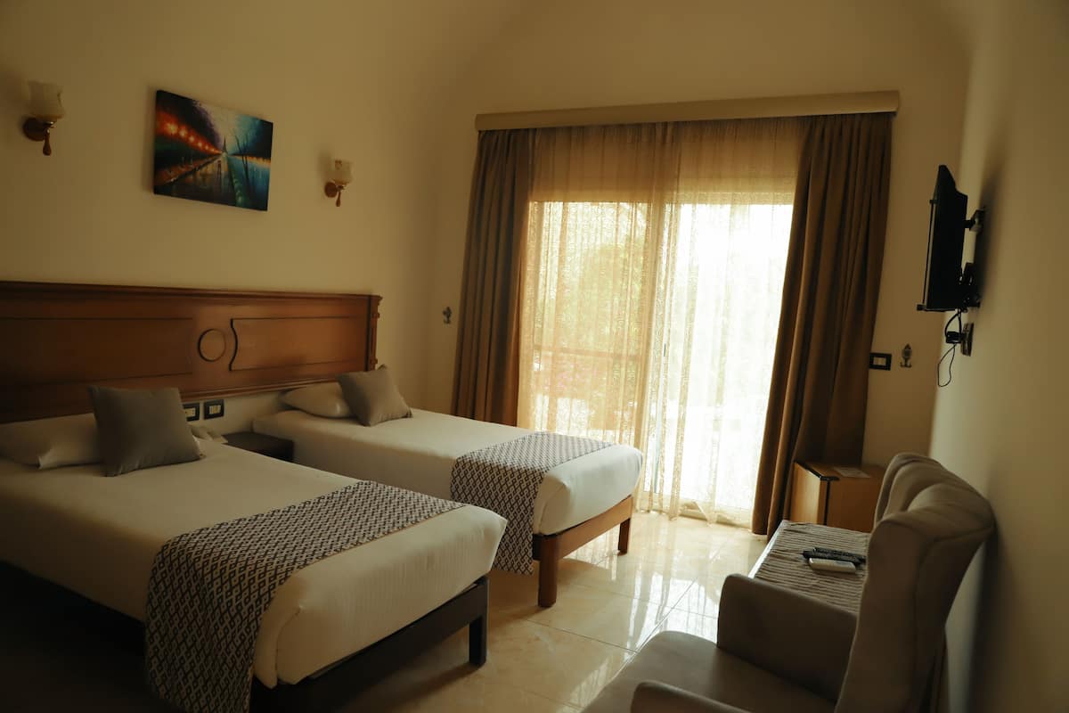 A hotel room with two beds, a TV, a desk, and a window with curtains.