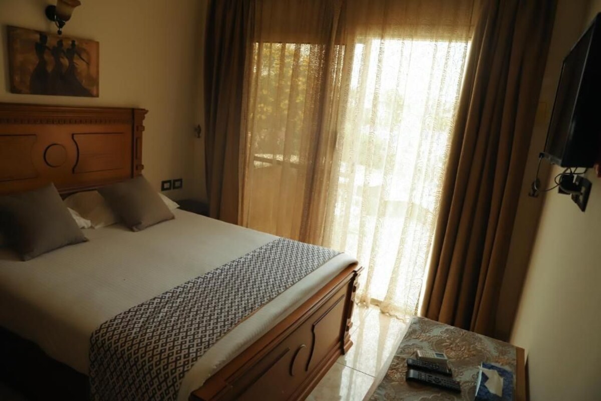A hotel room with a wooden bed, a bedside table, and a television mounted on the wall.