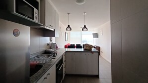 A compact kitchen with a microwave, sink, and two pendant lights. - Departamento con Piscina y Spa en la Serena (La Serena)