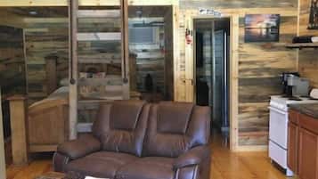 L’intérieur chaleureux d’un chalet avec un plancher en bois, un canapé en cuir marron, une table à manger et un coin cuisine équipé d’une cuisinière et de placards.
