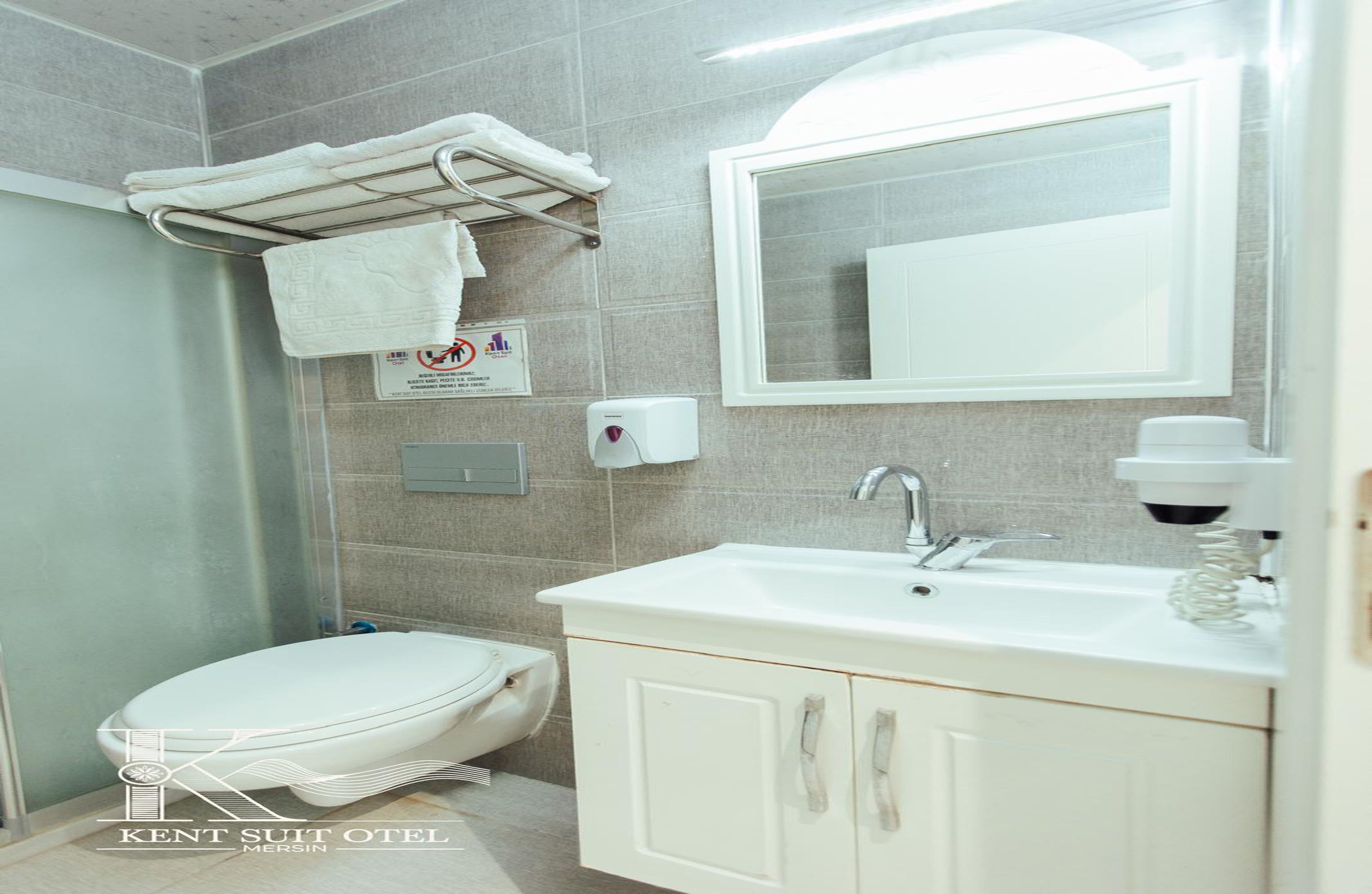 Baño con inodoro, lavabo, espejo, toallero y un cartel que indica que no se permite fumar.