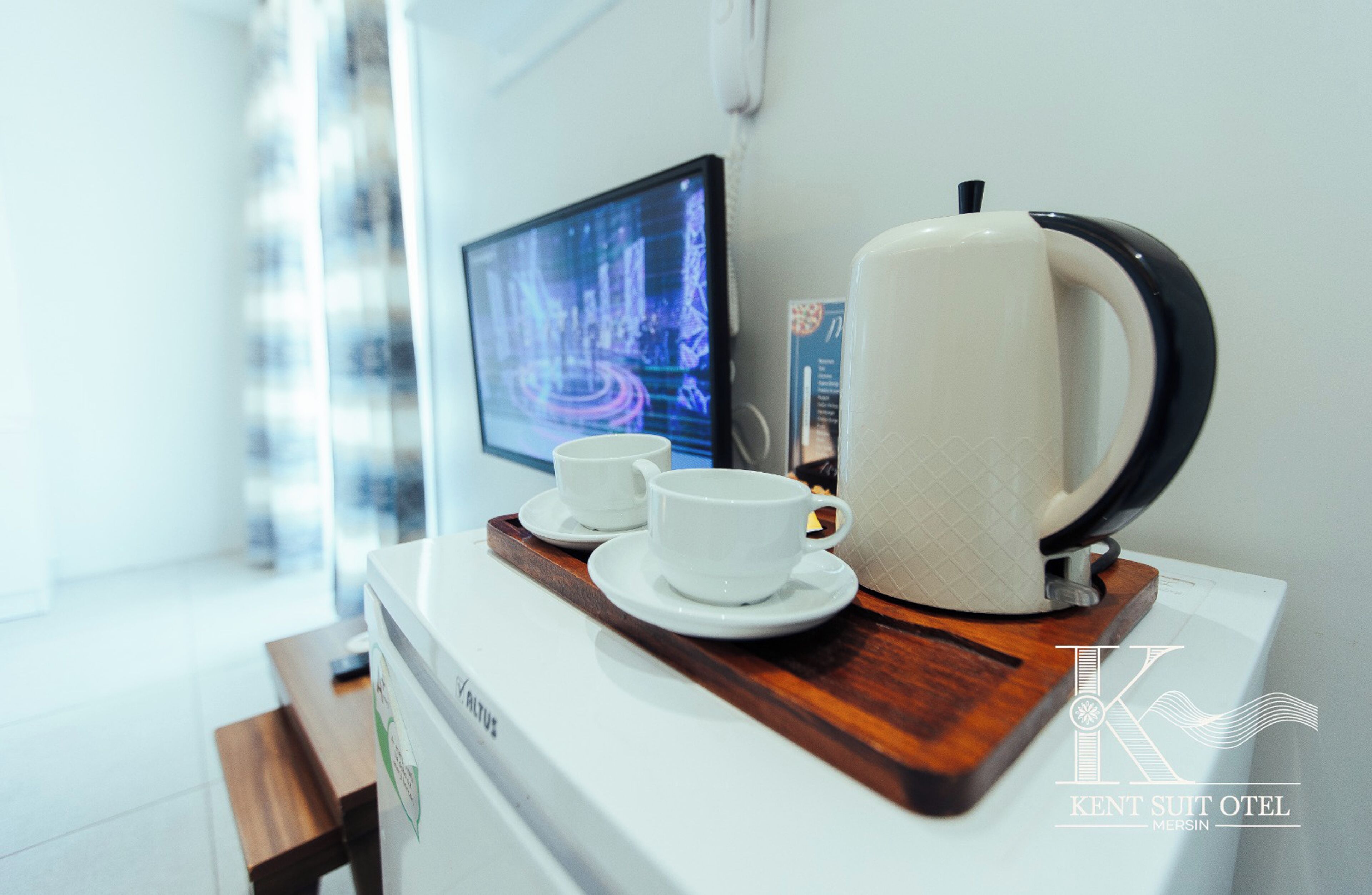 A kitchenette with a coffee maker, two cups, and a digital screen displaying a cityscape.