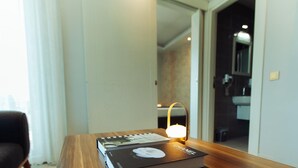 Una habitación de hotel con un escritorio de madera, un libro, una lámpara y un televisor en la pared.