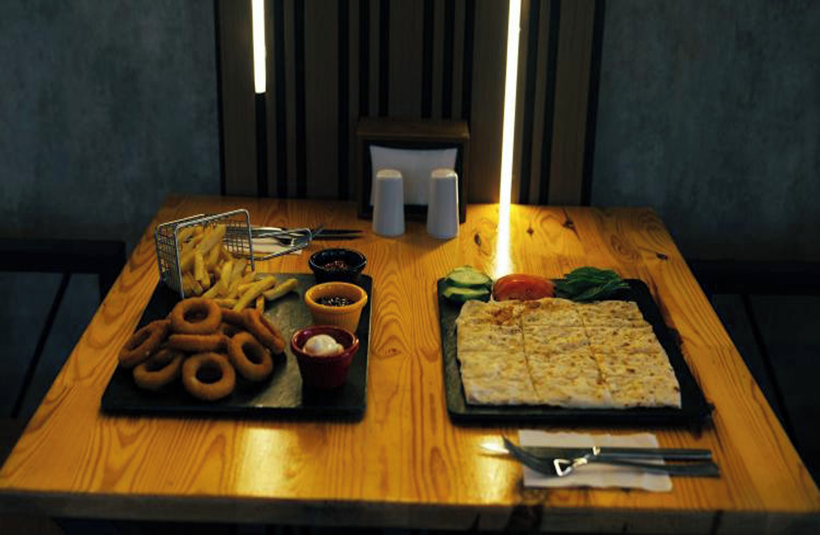 Una mesa de madera con diversos bocadillos, incluyendo pretzels, aros de cebolla y un sándwich grande.