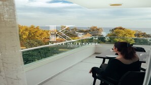 Una mujer sentada en una mesa en un balcón con vistas a árboles y al mar.