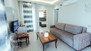 Una habitación de hotel moderna con sofá, una mesa de centro de madera, televisor y cama al fondo.