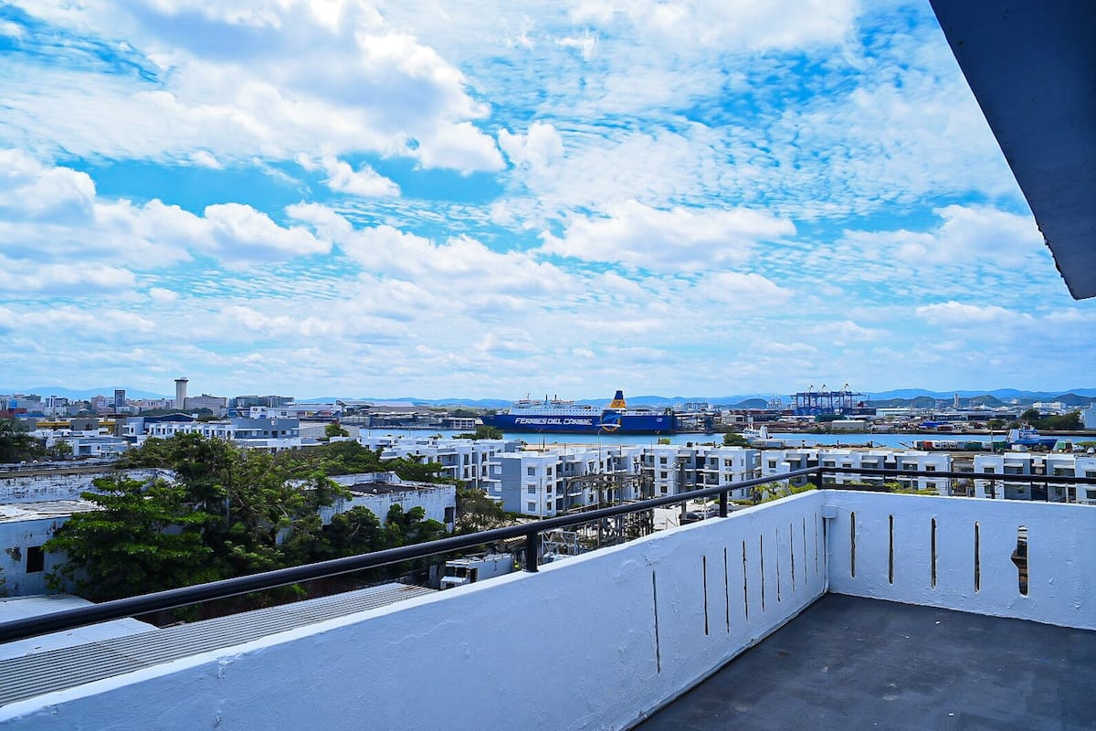 Une vue urbaine avec un grand navire nommé « FERRIES DEL CRISE » amarré dans un port, entouré de bâtiments et de verdure.