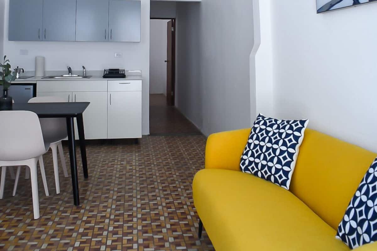 Un espace de vie moderne comprenant un canapé jaune, un coin repas et une cuisine.