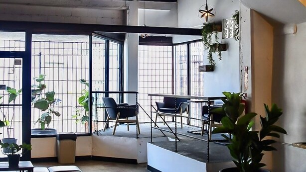 A modern interior with a high ceiling, large windows, and a mix of seating areas including a sofa and chairs. - La Ferreteria Apartments (San Juan)