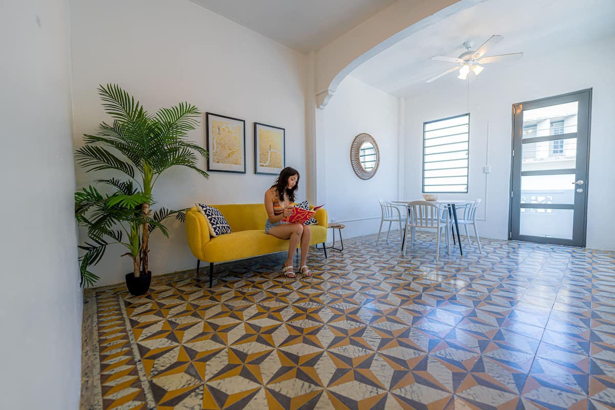 Une pièce avec un canapé jaune, une plante en pot et un sol orné d’un motif géométrique.