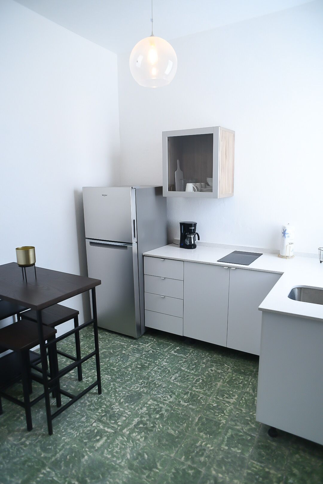 Una cocina compacta con refrigerador, cafetera, armario de madera y una mesa de comedor.