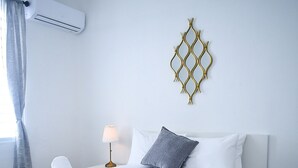 A neatly made bed with white linens, a decorative wall hanging, and a patterned floor. - La Ferreteria Apartments (San Juan)