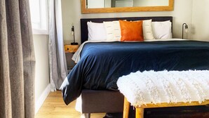 Un dormitorio con cama, mesita de noche, lámpara y un espejo grande en la pared.