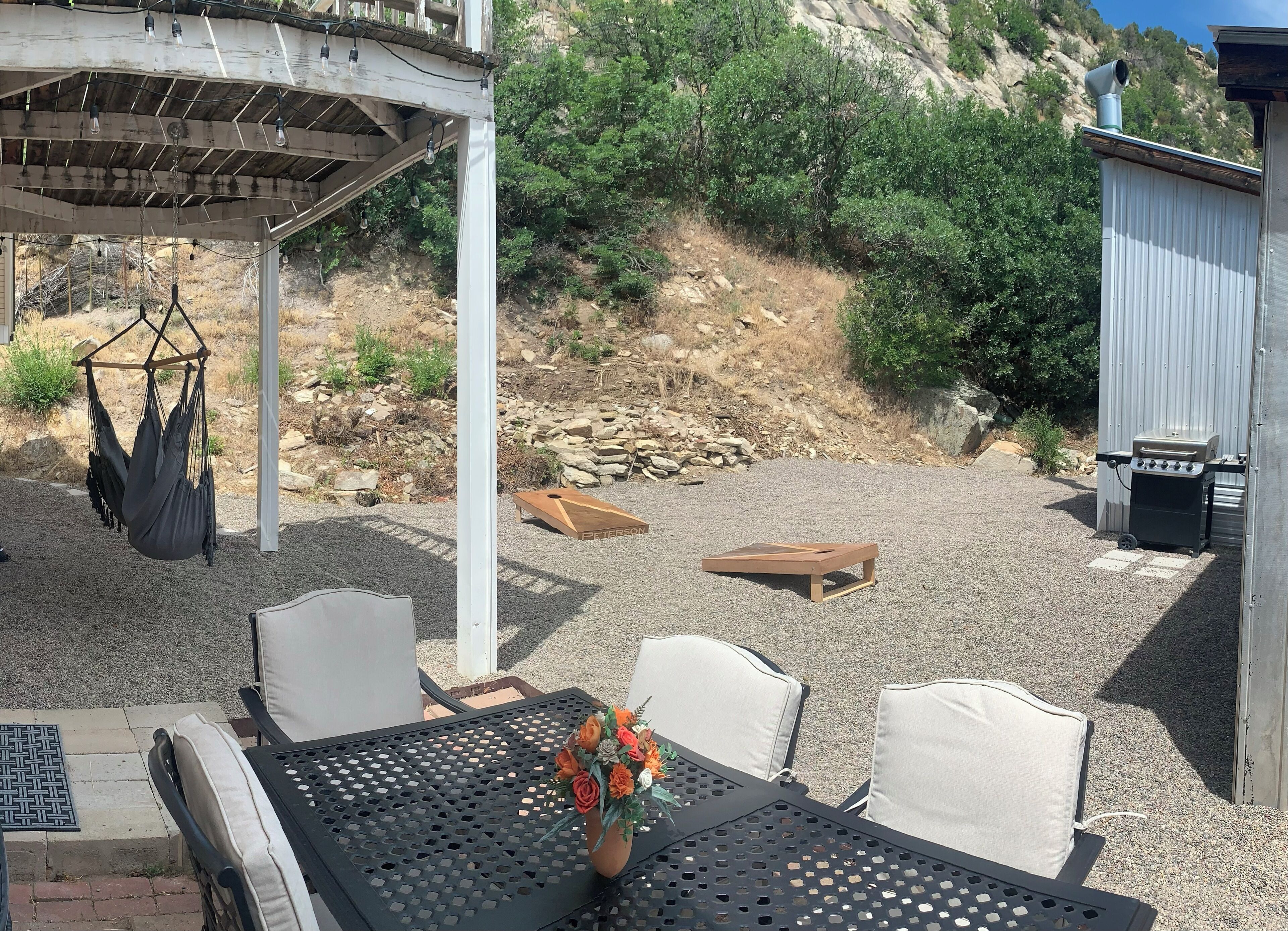 Une terrasse avec une table, des chaises, un fauteuil suspendu, un tabouret en bois et un espace barbecue.