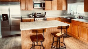 Una cocina moderna con armarios de madera, electrodomésticos de acero inoxidable, encimera de mármol y taburetes de bar.