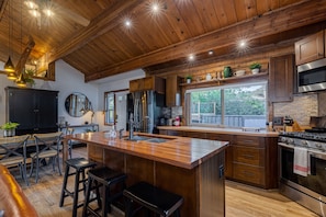 A spacious kitchen with a large island, wooden cabinets, stainless steel appliances, and a rustic ceiling. - Sonoma Wine Country Luxury Log Cabin (Sonoma)